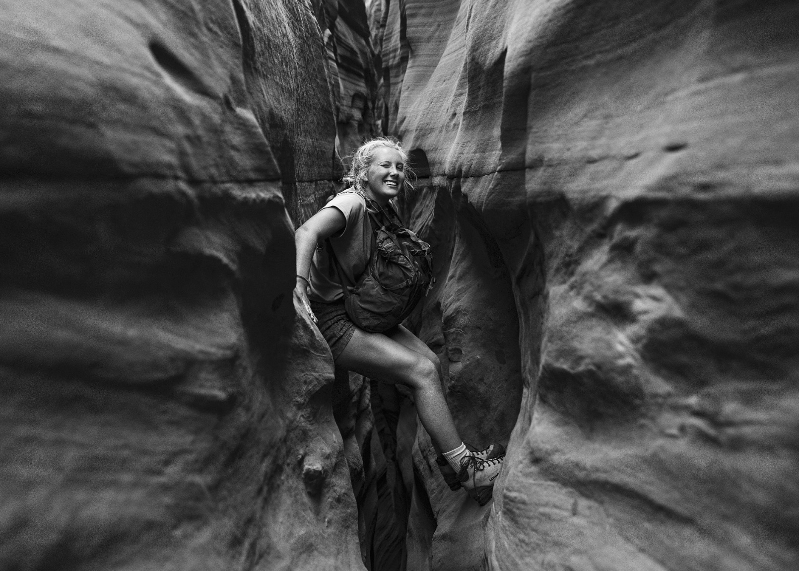 Black and white photo of woman climbing through canyon rock wall 